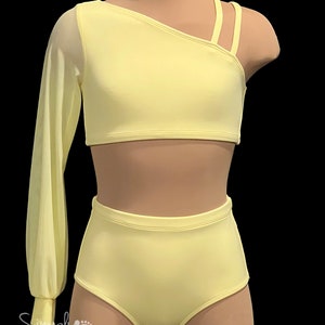 May include: A yellow dance outfit with a one-shoulder crop top and high-waisted shorts. The top has a long sheer sleeve on one side and three straps on the other shoulder. The shorts have a high waist and a fitted silhouette.