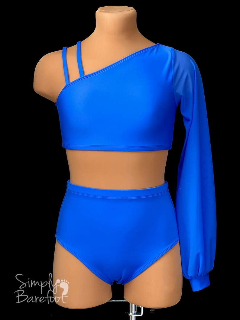 May include: A blue dance outfit with a one-shoulder crop top and high-waisted bottoms. The top has a long sleeve on one arm, made of sheer fabric. The outfit is on a mannequin.