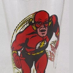 May include: A glass with a red and yellow illustration of The Flash, a superhero, running. The glass has a white background and the text "The Flash" is printed on the side.