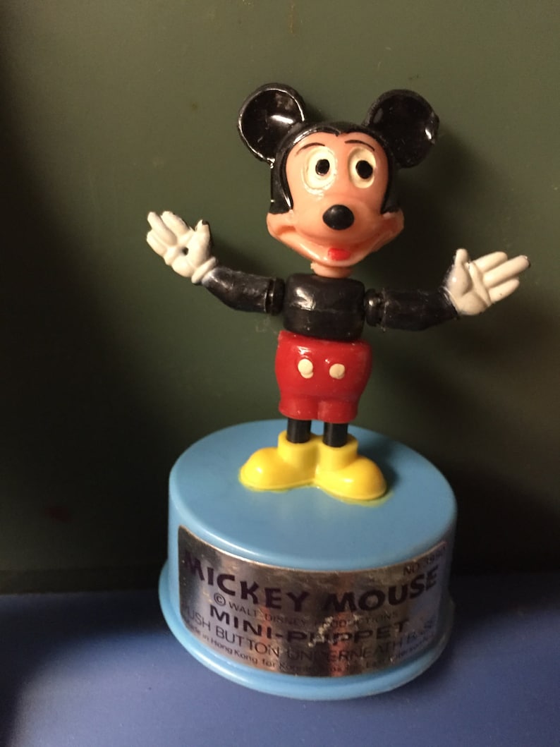 Pode incluir: Um brinquedo de mini-fantoche do Mickey Mouse vintage. A figura tem um torso e orelhas pretas, cal&ccedil;&otilde;es vermelhos, sapatos amarelos e luvas brancas. O fantoche est&aacute; em uma base azul clara com o texto "Mickey Mouse Mini-Puppet".
