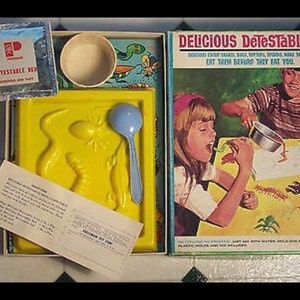 Puede incluir: Un juego vintage para niños llamado "Delicious Detestables!" con un molde de plástico amarillo de un insecto, una cuchara de plástico azul y una caja con ilustraciones coloridas de insectos. La caja incluye instrucciones para "¡Cómelos antes de que te coman!"