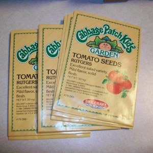 May include: A stack of yellow seed packets with a green Cabbage Patch Kids logo. The packets are for Rutgers tomato seeds and have a picture of red tomatoes. The text on the packet reads "Cabbage Patch Kids Garden Tomato Seeds Rutgers Excellent salad variety. Mild flavor, solid flesh. Net Wt. 50 mg. Skilcraft 4179-2900."