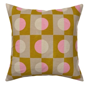 May include: Square cushion with a geometric pattern. The design features a grid of squares in mustard yellow and beige, with pink and white half-circles in each square. The cushion has a soft, textured appearance.