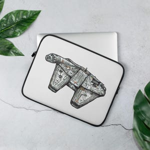 Könnte beinhalten: Eine weiße Laptoptasche mit einer detaillierten schwarz-grauen Tuschezeichnung eines Science-Fiction-Raumschiffs mit verwitterten Texturen und orangefarbenen Akzenten. Die Tasche hat einen schwarzen Reißverschluss und liegt auf einem silbernen Laptop.