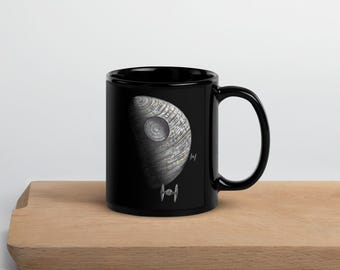 May include: A black ceramic coffee mug with a white image of the Death Star from Star Wars. The Death Star is partially obscured by a black TIE fighter.