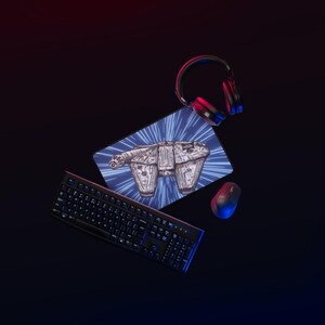 Op de afbeelding: Een zwart computertoetsenbord, een zwarte draadloze muis en een zwarte hoofdtelefoon gerangschikt rond een rechthoekige muismat met een grafische illustratie van een ruimteschip in de hyperruimte met blauwe en witte lichtstrepen.