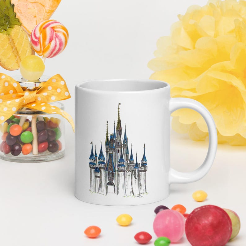 May include: White ceramic mug with a black and white line drawing of Cinderella's castle on the front. The castle is surrounded by a light blue sky.
