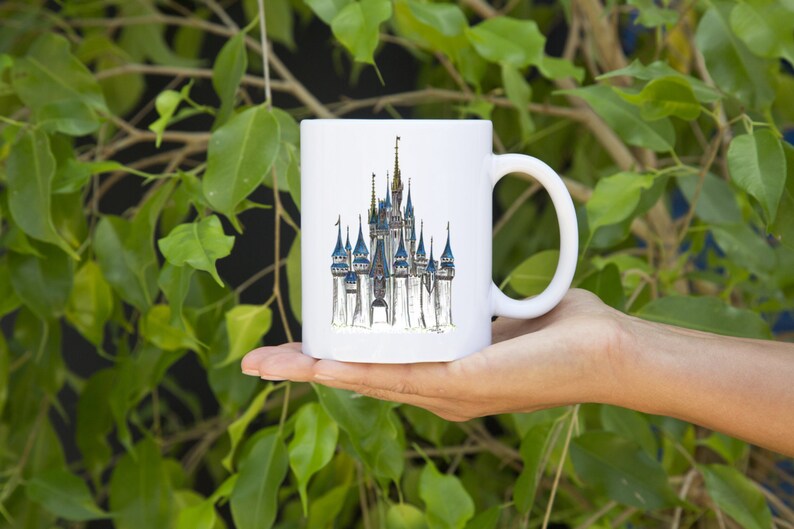May include: White ceramic mug with a hand-drawn illustration of Cinderella's castle in a whimsical style.