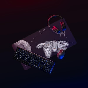 Può includere: Un tappetino da scrivania rettangolare con un'illustrazione a tema spaziale che mostra un'astronave dettagliata e una stazione spaziale sferica. Una tastiera nera, un mouse wireless nero e delle cuffie sono posizionati sul tappetino.