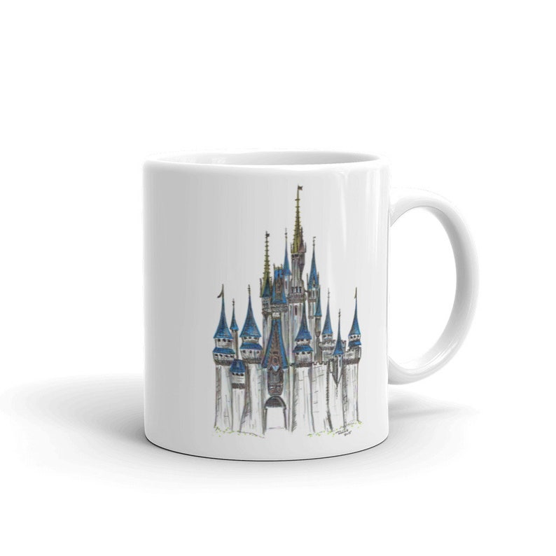 May include: White ceramic mug with a hand-drawn illustration of Cinderella's castle in a blue and gold color scheme.
