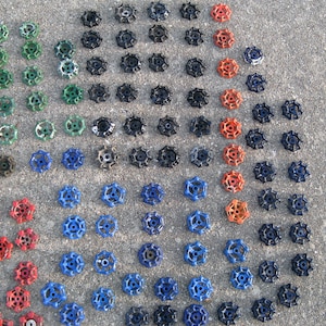 May include: A collection of vintage water valve handles arranged in a pattern on a concrete surface. The handles are in various colors, including blue, green, red, and black.