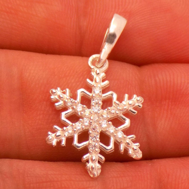 May include: A silver snowflake pendant with clear, sparkling crystals. The pendant is a winter-themed accessory, perfect for adding a touch of seasonal charm to any outfit. The snowflake design is intricate and detailed.