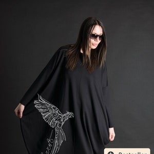 May include: Black oversized dress with a white parrot graphic and the word "Parrot" written in cursive. The dress is knee-length and has a loose fit. The model is wearing black heels.