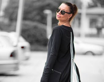 Puede incluir: Un vestido negro de manga larga con un detalle de cremallera blanca en la espalda. El vestido tiene una falda larga y fluida y se lleva con sandalias de tacón negras.