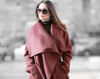 May include: A woman wearing a long, burgundy wrap coat with a large collar. She is wearing a plaid pattern on her legs and brown boots.
