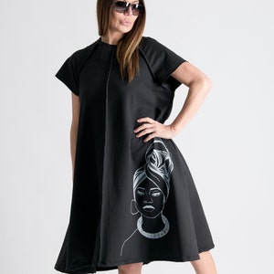 May include: A black knee-length dress with short sleeves and a white graphic of a woman's face on the side.