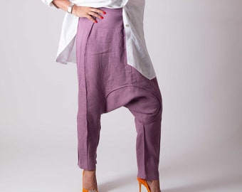 May include: A white long-sleeved button-down shirt, mauve drop-crotch trousers, a wide-brimmed hat with red and orange stripes, and orange high-heeled pumps with decorative embellishments. The outfit is completed with dark-tinted sunglasses.