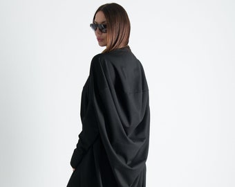 Pode incluir: Uma túnica preta de manga comprida com um design drapeado, usada com leggings pretos e sapatos pretos de salto alto.