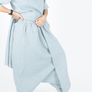 May include: A light blue linen wrap skirt with a wide waistband and a loose, flowing silhouette. The skirt is worn with white sneakers.