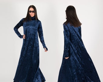 May include: A floor-length, dark blue velvet dress featuring a high turtleneck collar and long sleeves with thumbhole cuffs. The fabric has a crushed texture that reflects light, and the garment has a loose, flowing silhouette that reaches the floor.