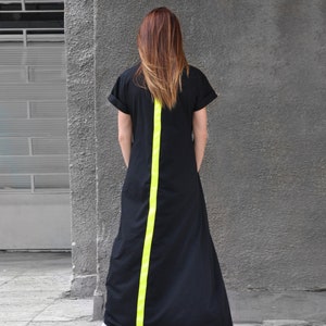 以下が含まれることがあります： 背中に明るい黄色のストライプが入った黒いマキシ丈ワンピースです。