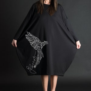 May include: A black oversized dress with a white parrot graphic and the word "Parrot" written in cursive. The dress is knee-length and has a loose fit.