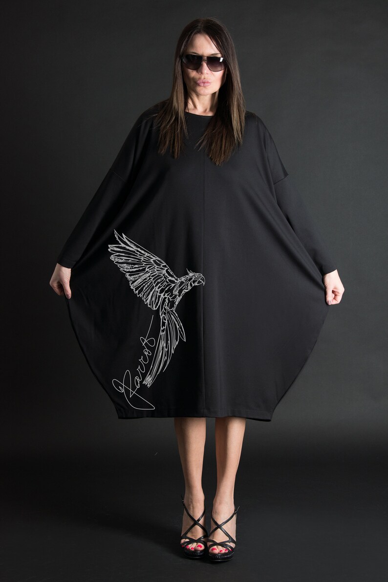 May include: A black oversized dress with a white parrot graphic and the word "Parrot" written in cursive. The dress is knee-length and has a loose fit.