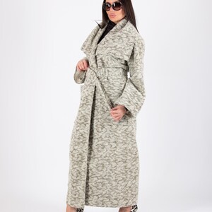 May include: A long, light gray patterned coat with a matching belt. The coat has wide sleeves and is paired with black and white patterned high heels. The background is plain white.
