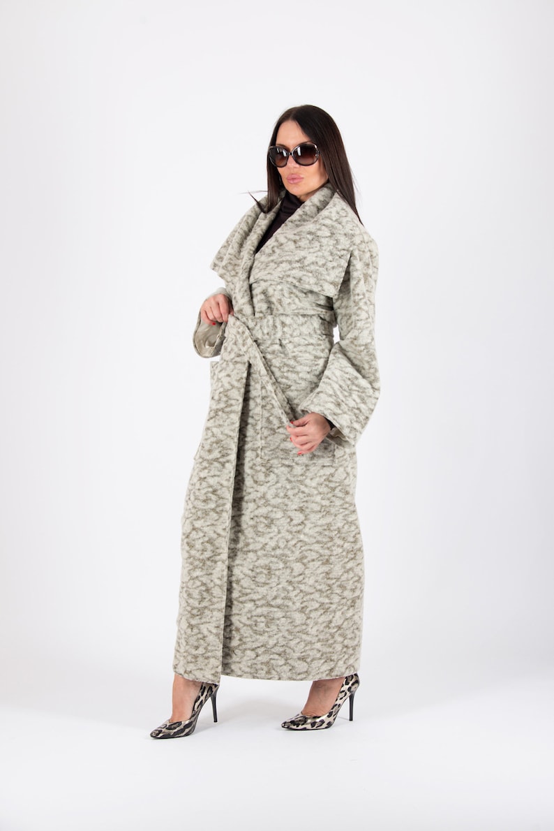 May include: A long, light gray patterned coat with a matching belt. The coat has wide sleeves and is paired with black and white patterned high heels. The background is plain white.