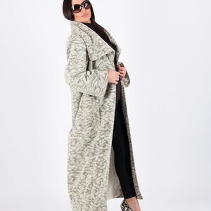 May include: A long, light-colored coat with a textured pattern. The coat is worn with black pants and leopard print heels. The coat has a wide collar and a flowing design. The person is wearing sunglasses.
