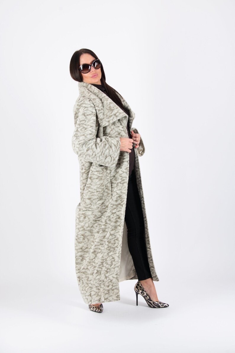 May include: A long, light-colored coat with a textured pattern. The coat is worn with black pants and leopard print heels. The coat has a wide collar and a flowing design. The person is wearing sunglasses.