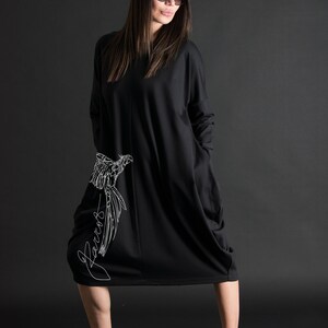 May include: A black long-sleeved dress with a white bird design and the word "Parrot" written on the side. The dress has a loose fit and a slightly gathered hemline.