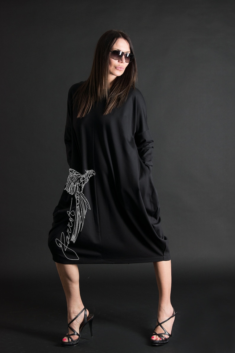 May include: A black long-sleeved dress with a white bird design and the word "Parrot" written on the side. The dress has a loose fit and a slightly gathered hemline.