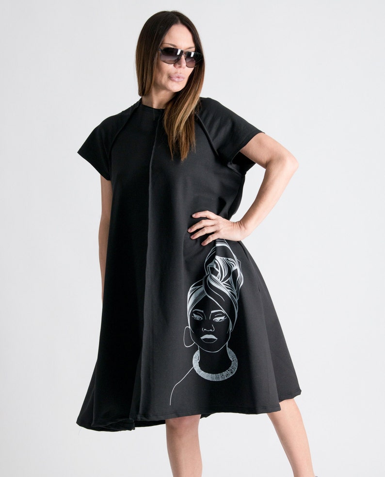 May include: A black knee-length dress with short sleeves and a white graphic of a woman's face on the side.