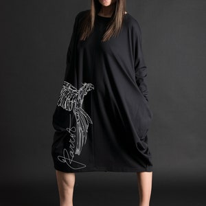 May include: A black long-sleeved dress with a white parrot graphic and the word "Parrot" written in cursive on the side. The dress has a loose fit and a large pocket on each side.