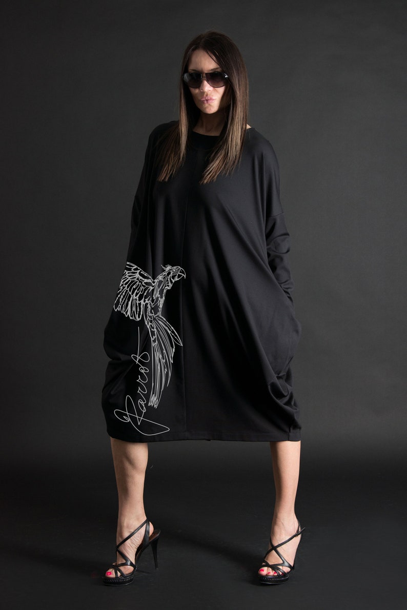 May include: A black long-sleeved dress with a white parrot graphic and the word "Parrot" written in cursive on the side. The dress has a loose fit and a large pocket on each side.