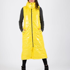 May include: A long yellow puffer vest with a zipper closure and a high collar. The vest has a shiny finish and is quilted.