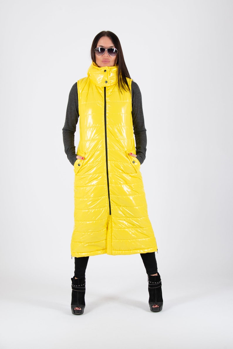 May include: A long yellow puffer vest with a zipper closure and a high collar. The vest has a shiny finish and is quilted.