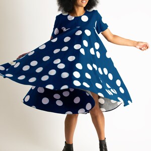 May include: A navy blue dress with large white polka dots. The dress has short sleeves and a flared skirt, and is being twirled. The person in the image is wearing black sunglasses and black high-heeled sandals.