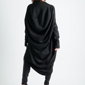 May include: A black long-sleeved tunic with a draped design. The tunic is worn with black leggings and black high-heeled shoes.