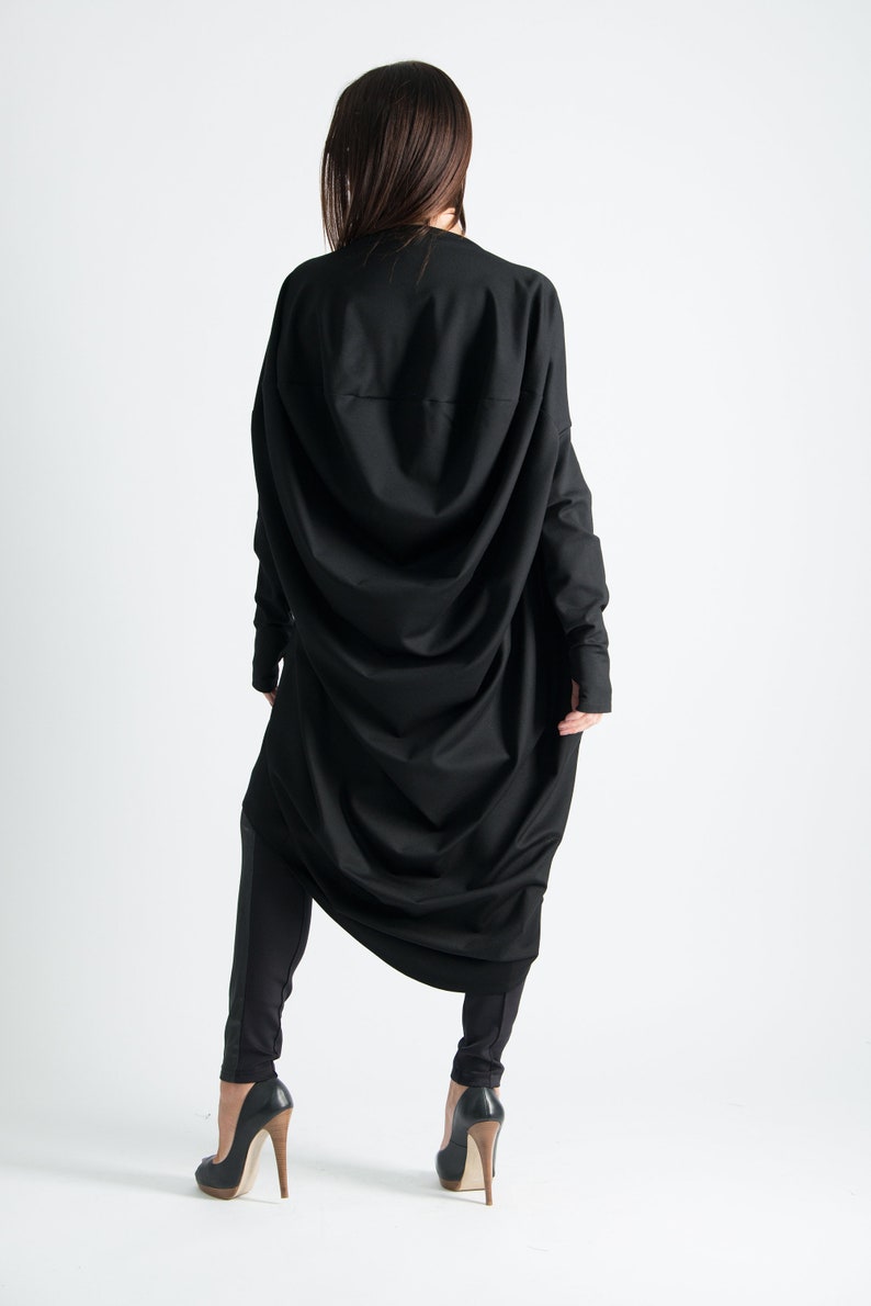 May include: A black long-sleeved tunic with a draped design. The tunic is worn with black leggings and black high-heeled shoes.