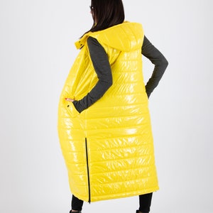 May include: A long yellow puffer vest with a hood. The vest has a shiny finish and is quilted with horizontal lines. The vest is sleeveless and has a zipper down the front.