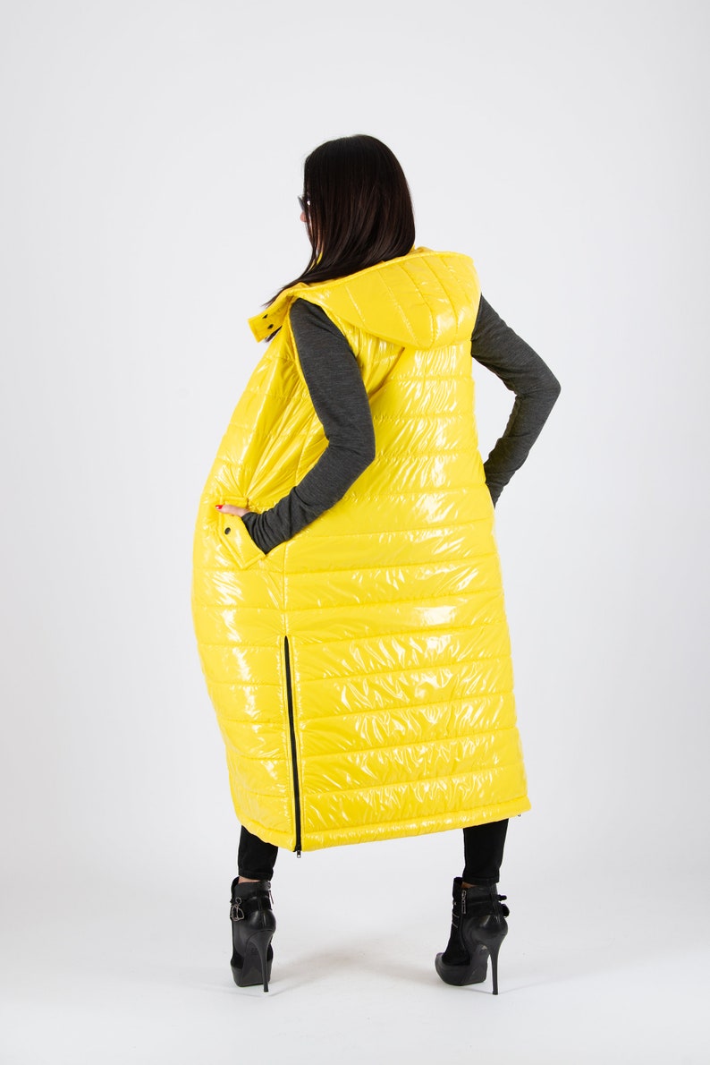 May include: A long yellow puffer vest with a hood. The vest has a shiny finish and is quilted with horizontal lines. The vest is sleeveless and has a zipper down the front.