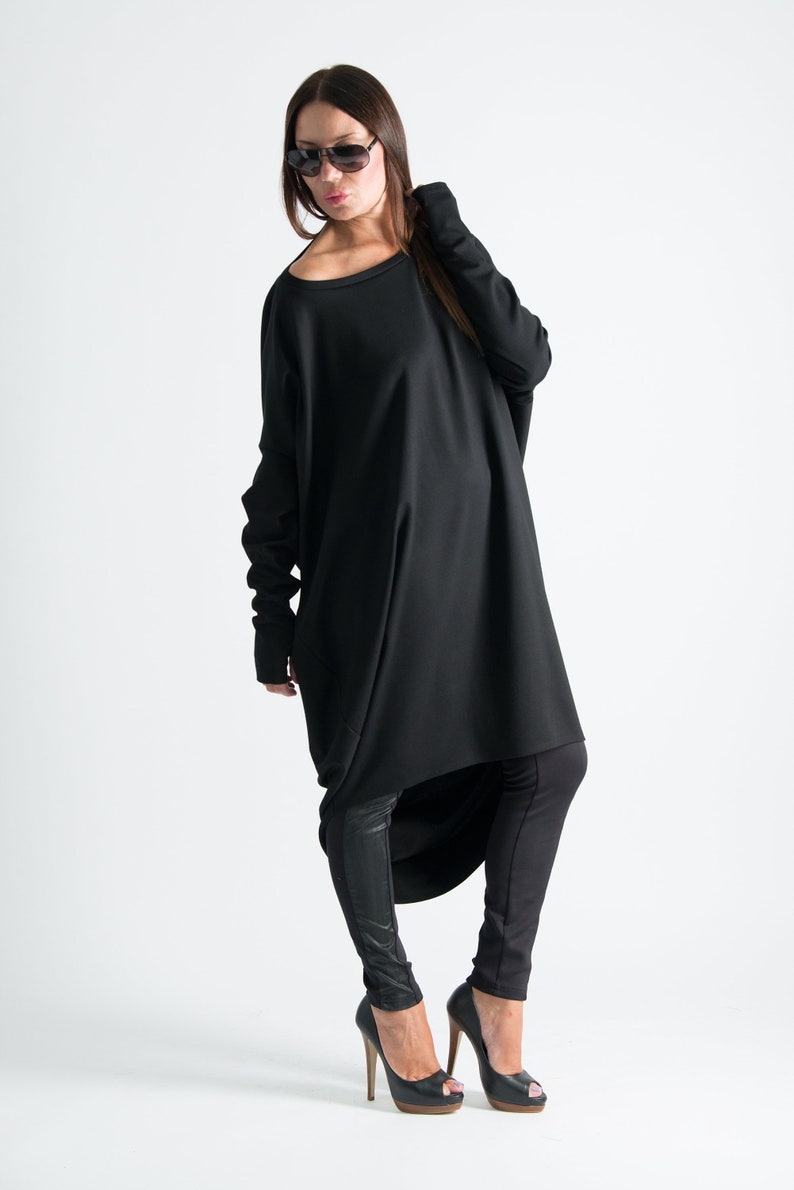 May include: A black long-sleeved tunic with a high-low hemline. The tunic is worn with black leggings and black high-heeled shoes.
