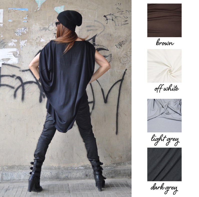 May include: A woman wearing a black oversized top with a draped neckline, black pants, and black ankle boots. She is standing in front of a graffiti-covered wall. The image also shows swatches of fabric in brown, off-white, light grey, and dark grey.