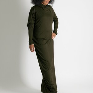 May include: A woman wearing a long, dark green, form-fitting dress with a high neckline and long sleeves. She is wearing black sunglasses and black high-heeled sandals.