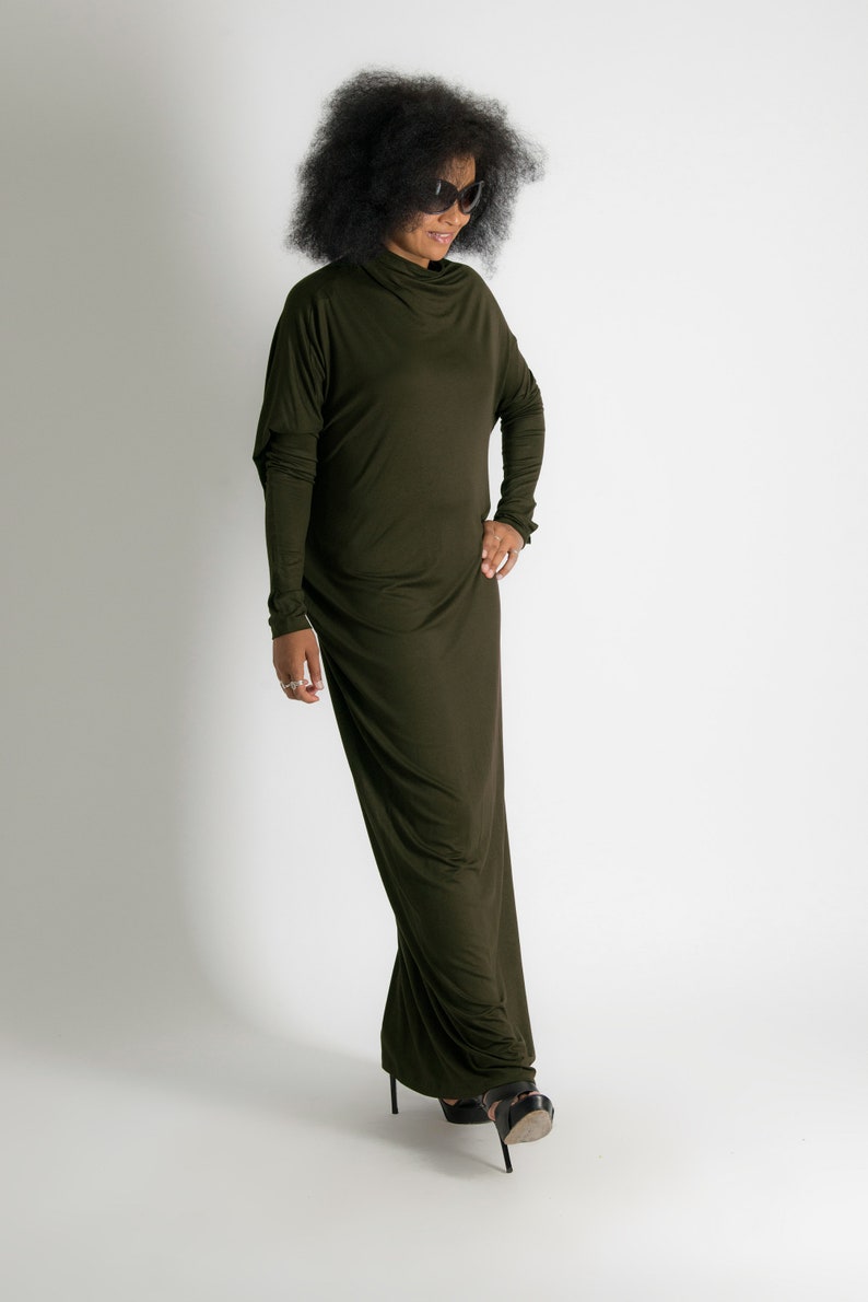 May include: A woman wearing a long, dark green, form-fitting dress with a high neckline and long sleeves. She is wearing black sunglasses and black high-heeled sandals.
