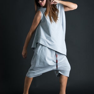 K&ouml;nnte beinhalten: Eine Frau tr&auml;gt einen grauen, &auml;rmellosen Jumpsuit mit einem schwarzen G&uuml;rtel, auf dem "LOVE LOVE LOVE" in roten Buchstaben steht. Sie tr&auml;gt eine Sonnenbrille und hat ihr Haar offen.