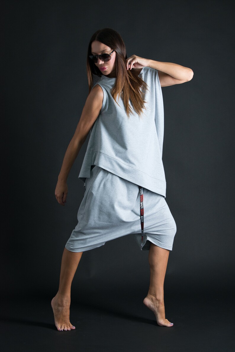 K&ouml;nnte beinhalten: Eine Frau tr&auml;gt einen grauen, &auml;rmellosen Jumpsuit mit einem schwarzen G&uuml;rtel, auf dem "LOVE LOVE LOVE" in roten Buchstaben steht. Sie tr&auml;gt eine Sonnenbrille und hat ihr Haar offen.