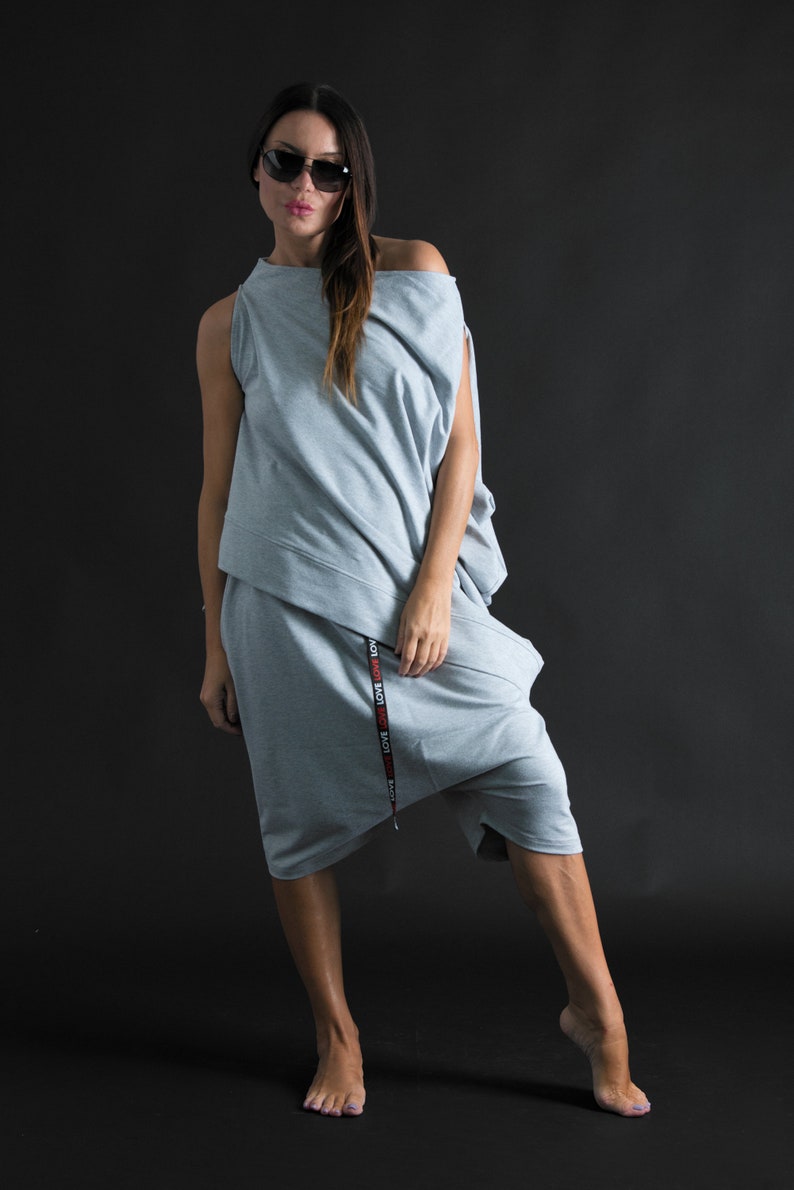 K&ouml;nnte beinhalten: Ein grauer, einseitiger, locker sitzender Jumpsuit mit einem schwarzen und roten "LOVE"-Druck an der Seite. Der Jumpsuit hat einen langen, flie&szlig;enden Rock und ein figurbetontes Oberteil.
